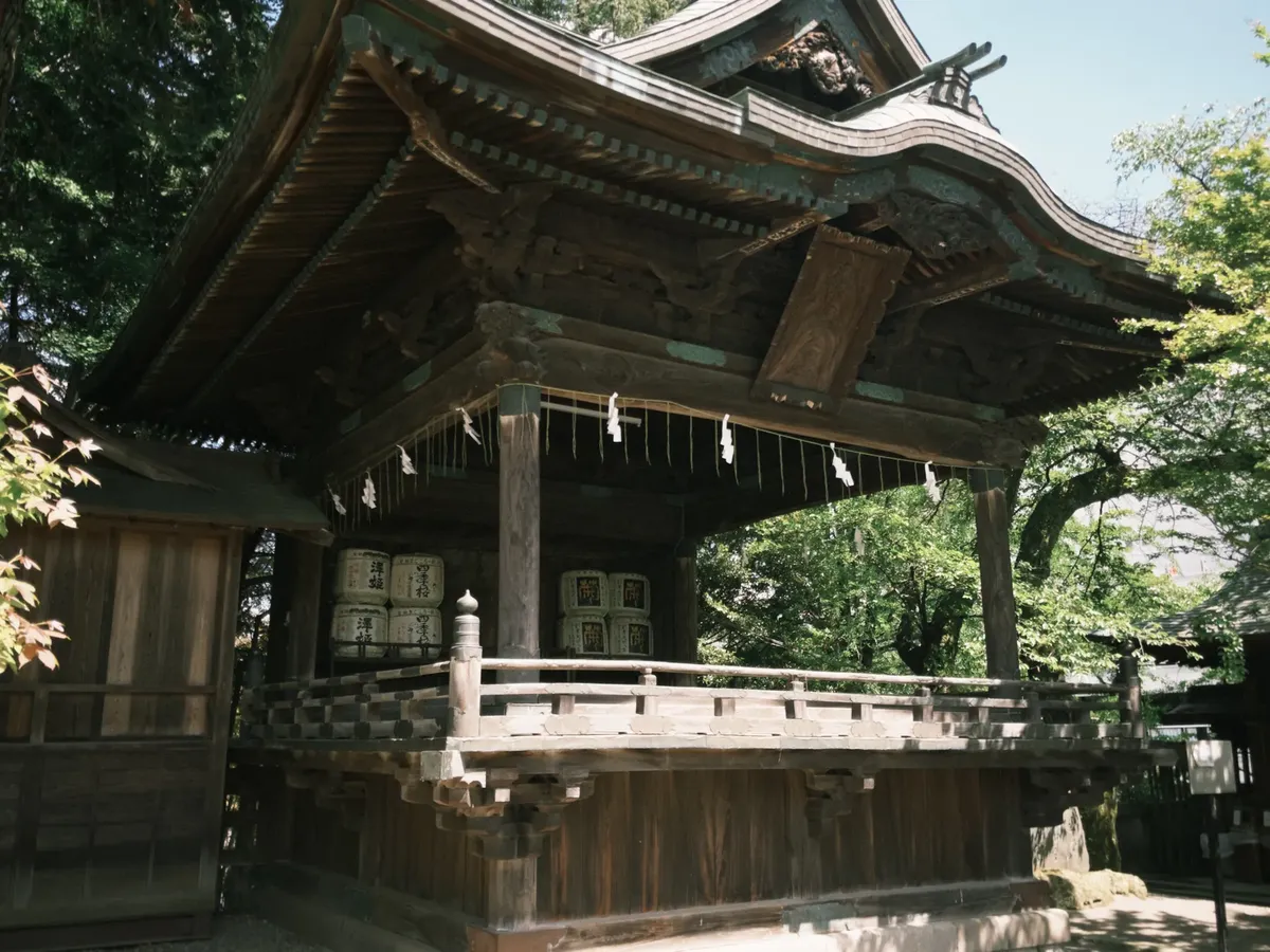 A wooden Japanese shrine surrounded by lush forest greenery under a clear sky.