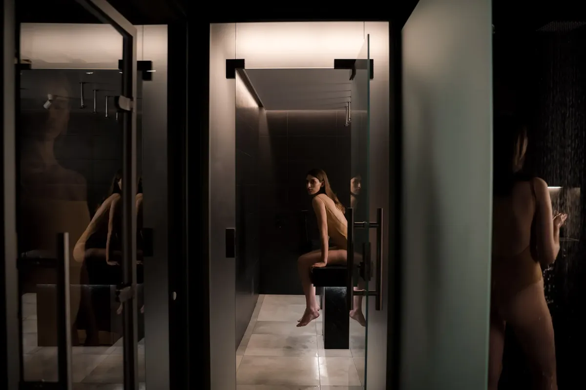 A serene spa environment with a woman in a swimsuit, reflected in a shower setting, capturing calmness and luxury.